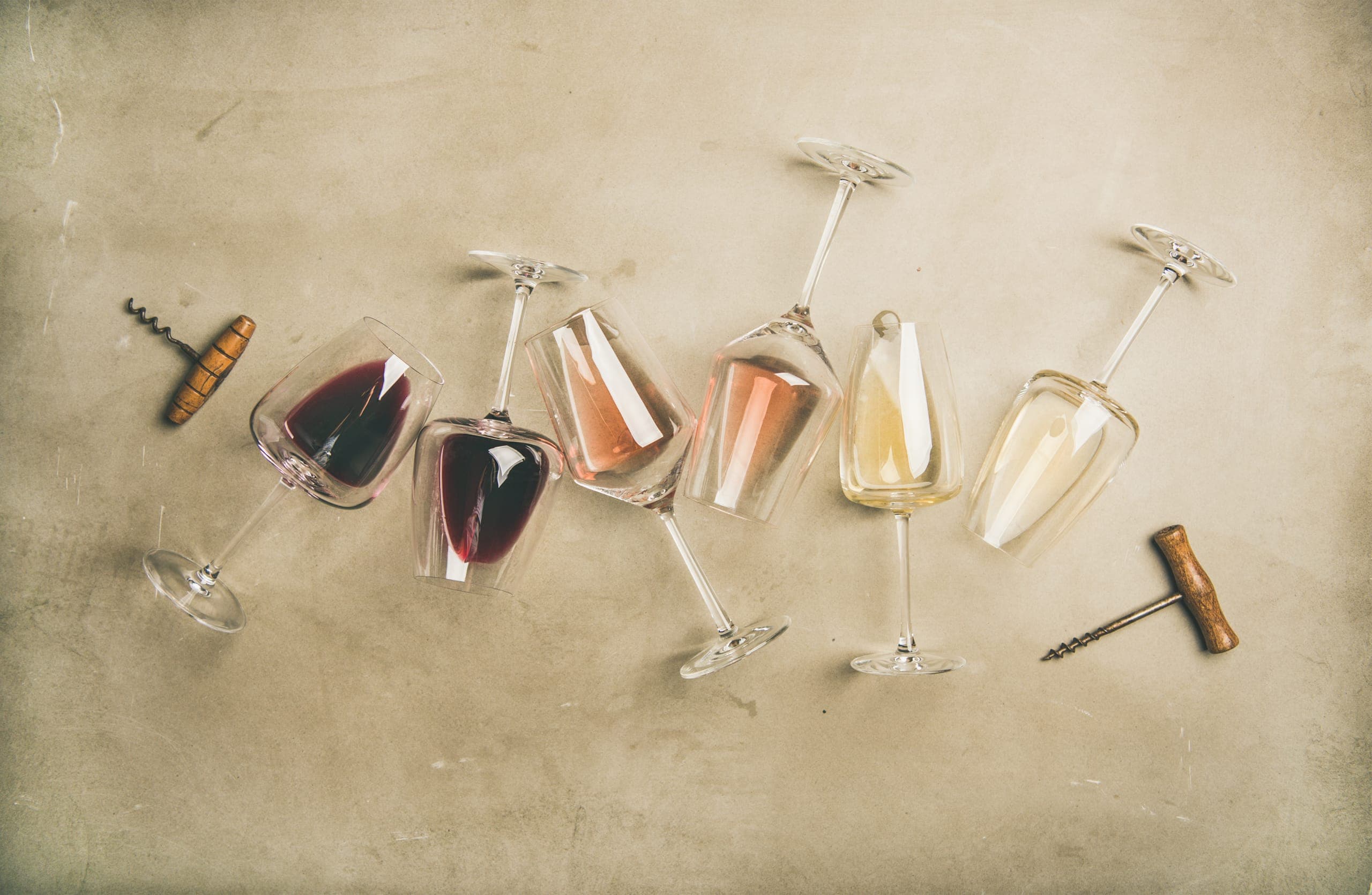 Red wine, rosé and white wine in glasses lying on concrete, next to two old corkscrews