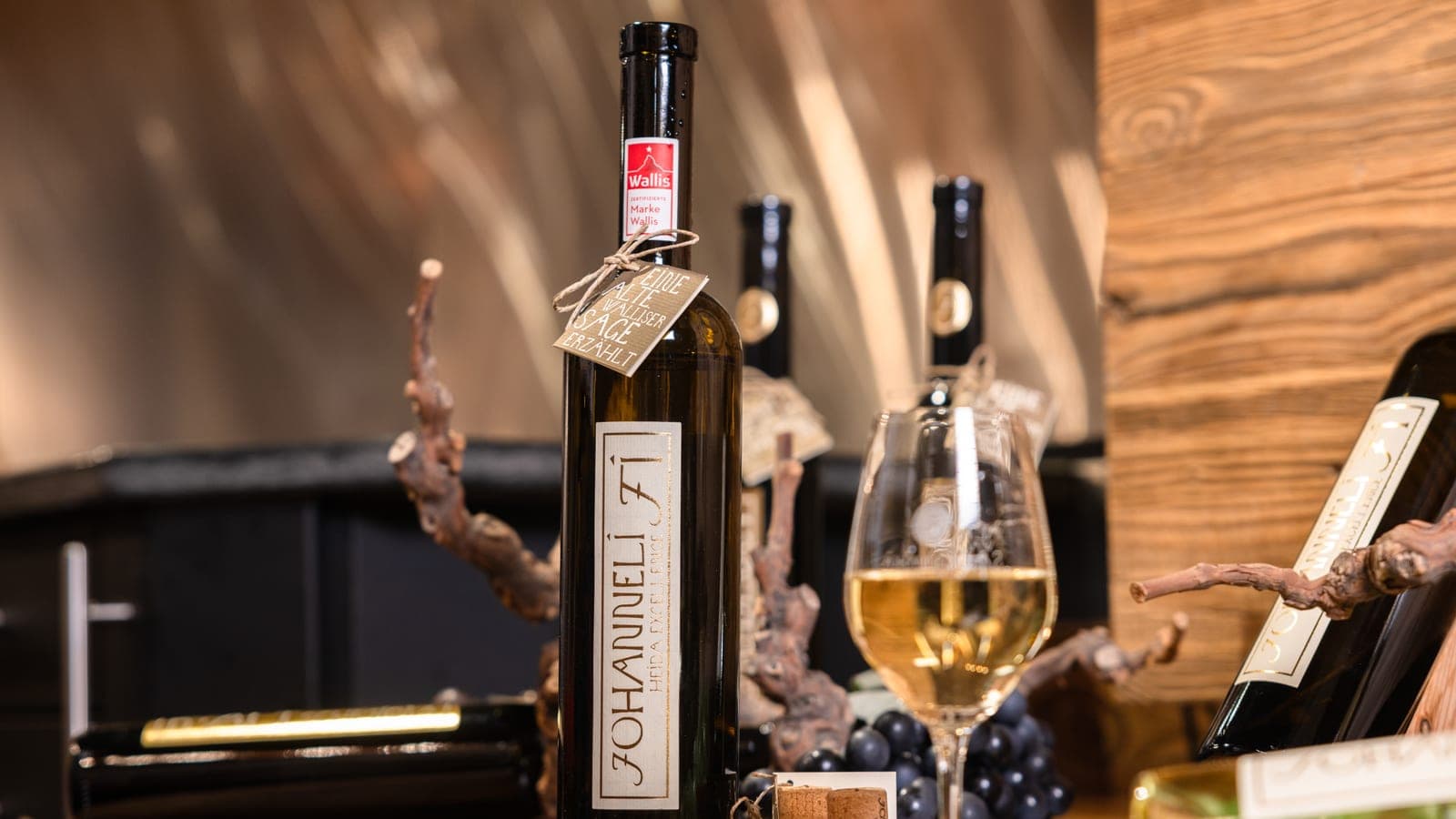 Bouteille de Johanneli Fi Heida Excellence AOC Valais, le vin blanc phare de la maison, avec le label de qualité «Marke Wallis», à côté d'un verre de vin blanc (Photo: levin.studio)