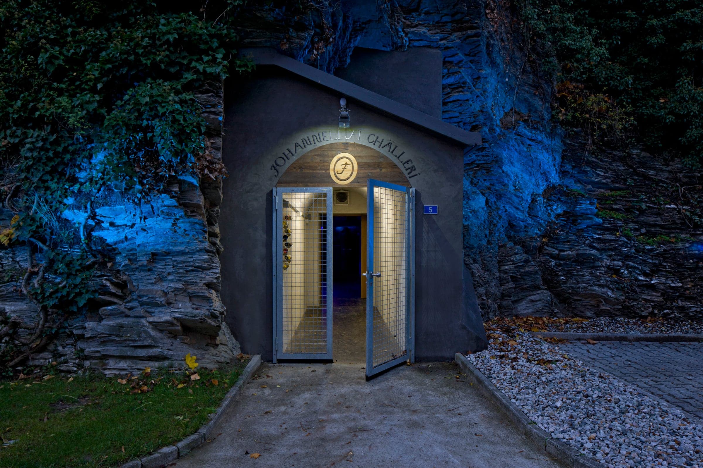 Illuminated entrance to the Johanneli Fi Weinkeller in Visp, cut directly into the rock